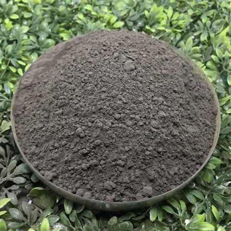 Round container filled with dark soil on a green leafy background
