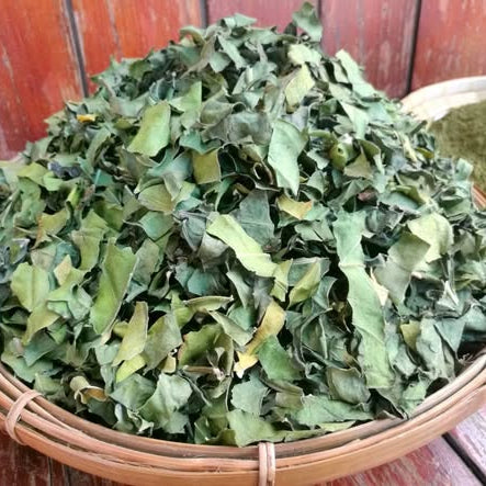 Dried green leaves in a woven basket on a wooden surface