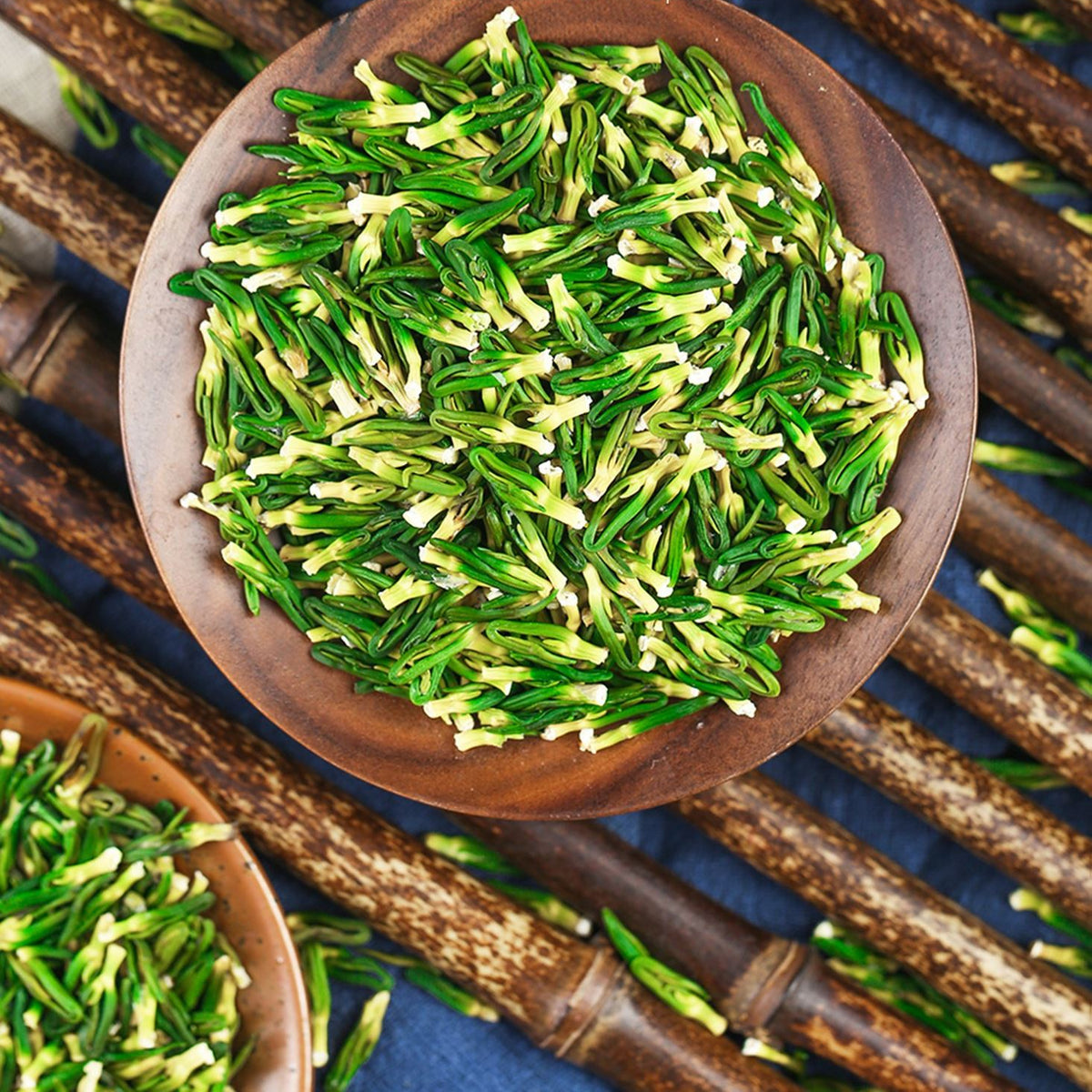 Green tea leaves in a wooden bowl with CHARMCHA branding on a blue background