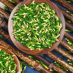Green tea leaves in a wooden bowl with CHARMCHA branding on a blue background